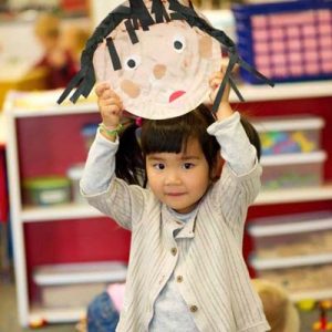 a child holding up a self portrait at a preschool